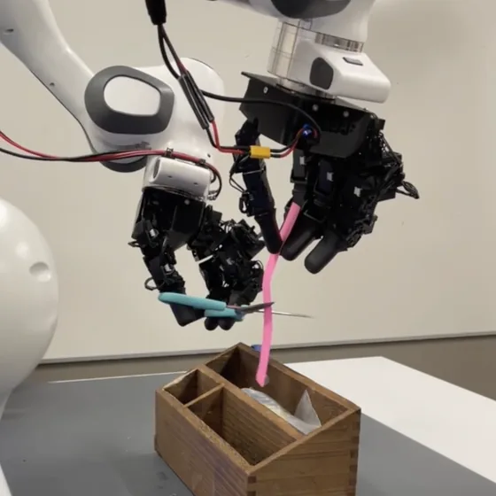 Two dexterous robot hands cutting a length of pink tape with scissors